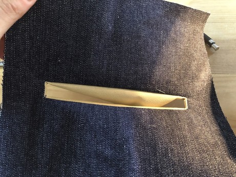 A rectangular hole for a zipper in the denim front face of the bag. The canvas lining shows through.